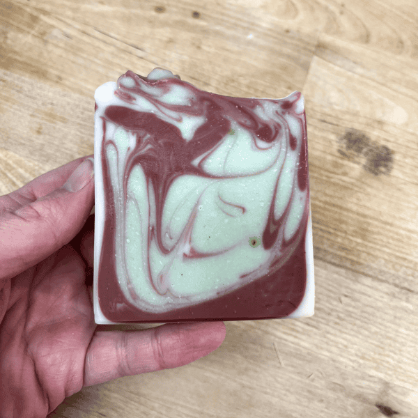 hand holding peppermint candy tallow bar soap. Red, green, and white swirl