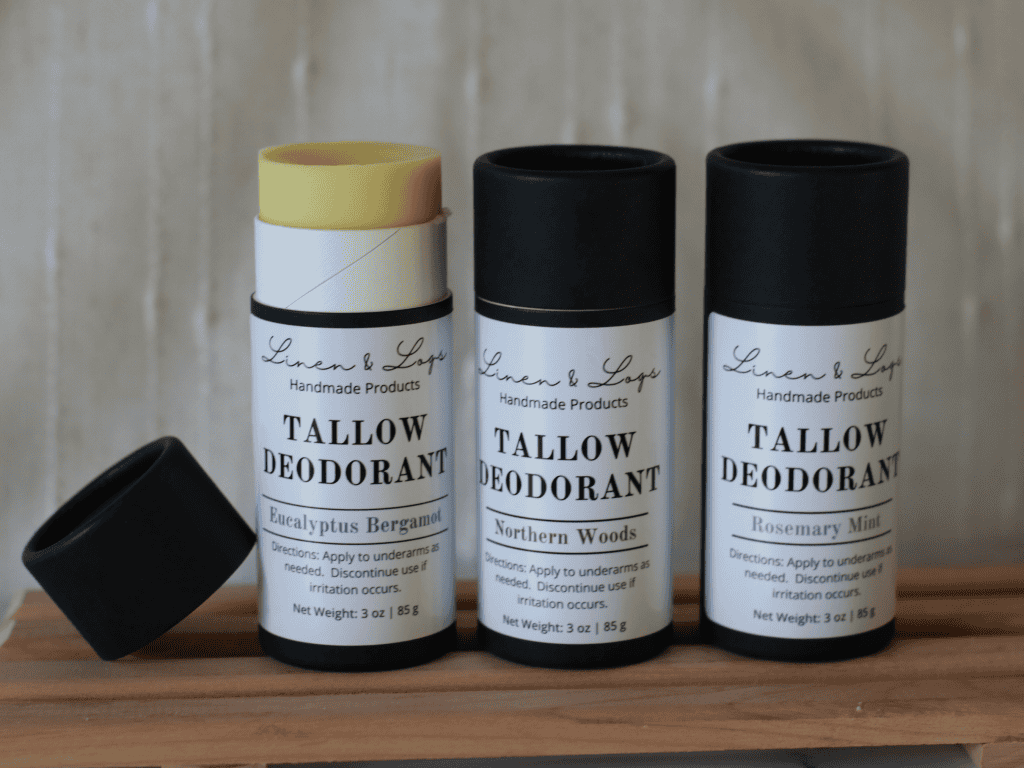 three Linen and Logs deodorants inblack biodegradable tubes with white labels sitting on a multibar slat holder. Far left deodorant has lid off and leaning on the side. and the deodorant is sticking up. The other two deodorants have their lids on.
