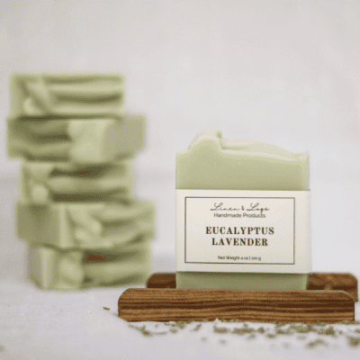 bar of eucalyptus lavender tallow soap sitting on a wood soap holder with a stack of 5 soaps in the background and lavender sprinkled in front