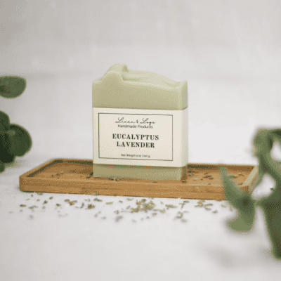 bar of eucalyptus lavender tallow soap sitting on a wood tray with faux eucalyptus leaves in corners - and lavender sprinkled in front