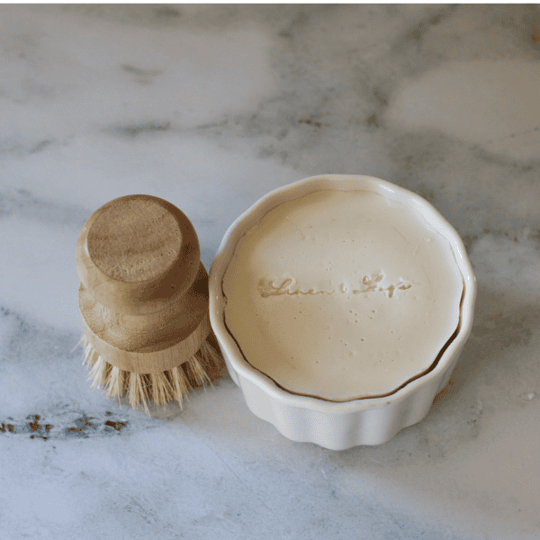 solid dish soap in a white ramekin with a dish brush on the left side