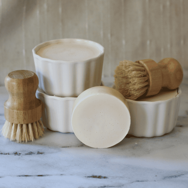 Solid dish soap in white ramekins and dish scrub brushes with one kitchen dish soap refill bar.