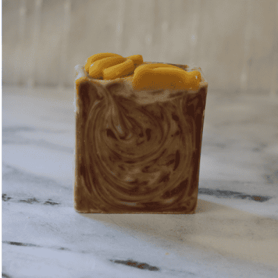 A single bar of sweet orange and patchouli tallow soap with brown and yellow swirls and pumpkin embeds on top