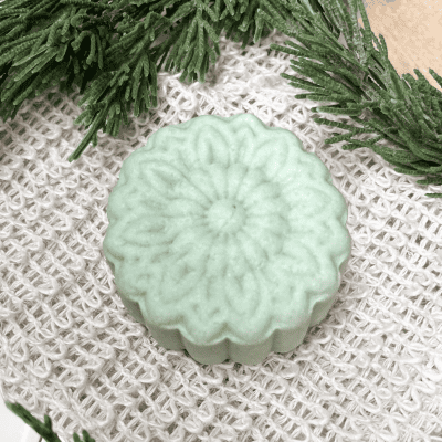 Shampoo bar laying on a sisal glove with greenery on the upper edge