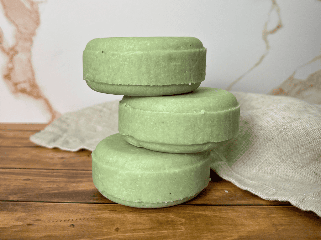 stack of 3 linen and logs shampoo bars in a light green color on a wood like table with a marble looking background