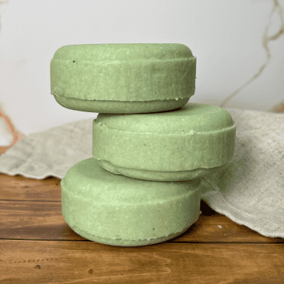 stack of 3 linen and logs shampoo bars in a light green color on a wood like table with a marble looking background
