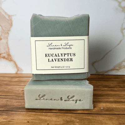 a bar of eucalyptus lavender soap sitting on top of another bar of soap. Shows the label and Linen & Logs soap stamp on bars of soap