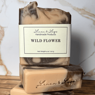 bar of Wild Flower Tallow Soap sitting on top of another bar of soap. Colored with pink clay and purple alkanet root infused olive oil.